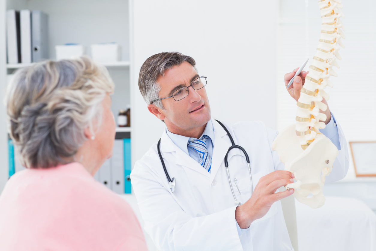 Male doctor explaning anatomical spine to senior woman in clinic